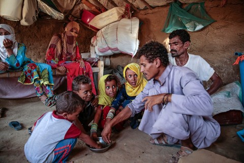 adults and children crouching to eat Halas from a common bowl