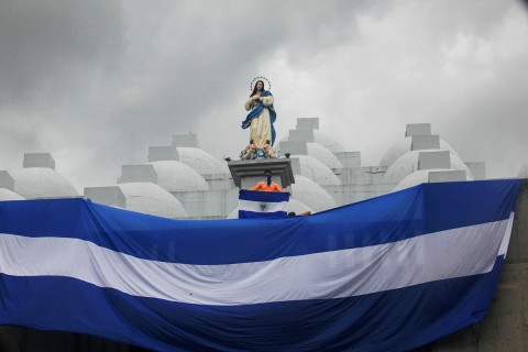 A masked youth holds a Nicaraguan national flag while standing on the roof of the Cathedral in Managua, Nicaragua.