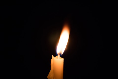 a mostly melted candle burning against a dark background