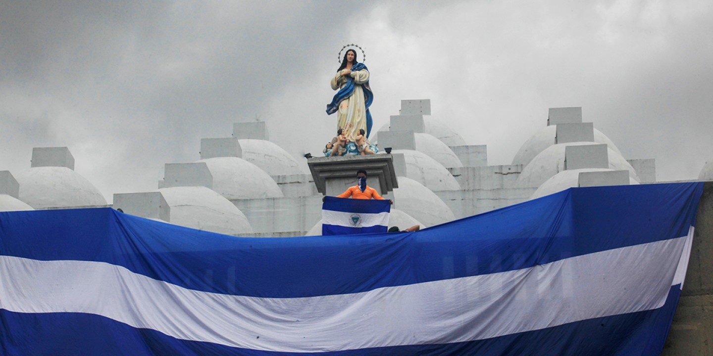 A masked youth holds a Nicaraguan national flag while standing on the roof of the Cathedral in Managua, Nicaragua.