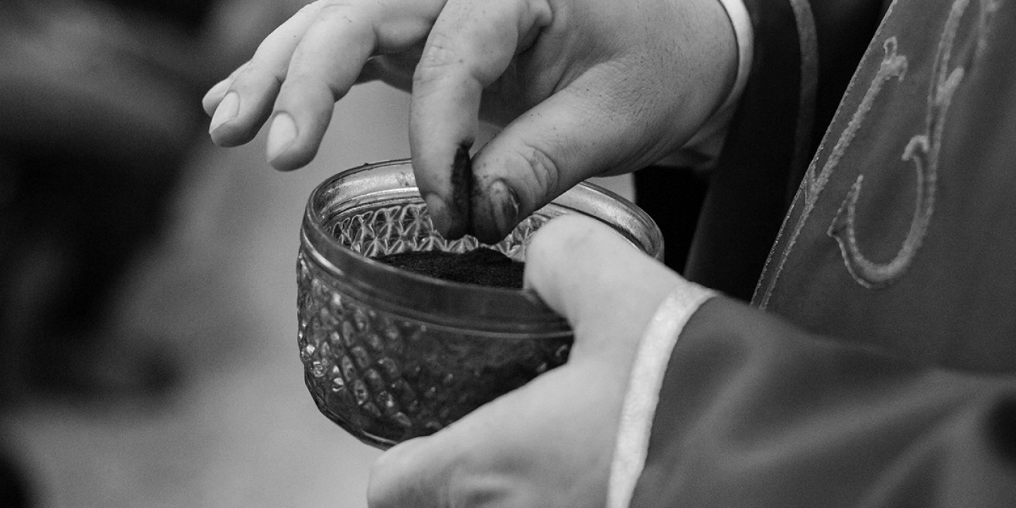 a robed clergy person holds a bowl of ashes, preparing for distribution at an Ash Wednesday service