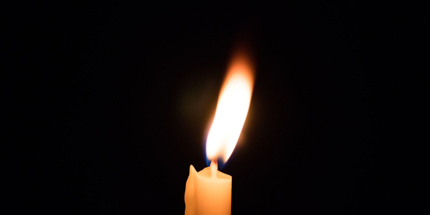 a mostly melted candle burning against a dark background